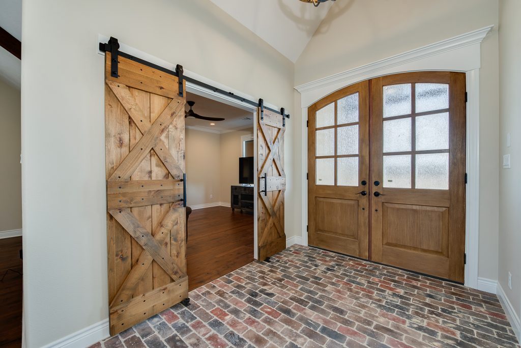 Entrance foyer of a custom built home with brick flooring and sliding barn doors.