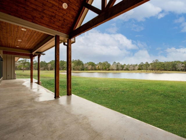 Rear porch of the WLS Custom Home with wood detailing and view of a lush lawn and water feature.