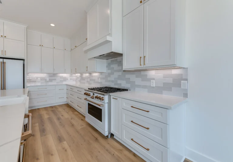 Modern kitchen with white cabinets and appliances, light brown wooden floors, and soft under-cabinet lighting for a warm, inviting ambiance.