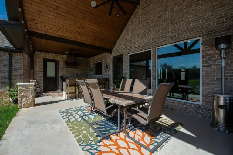 Covered patio with dining table, outdoor ceiling fan, and brick walls, designed for year-round outdoor living.