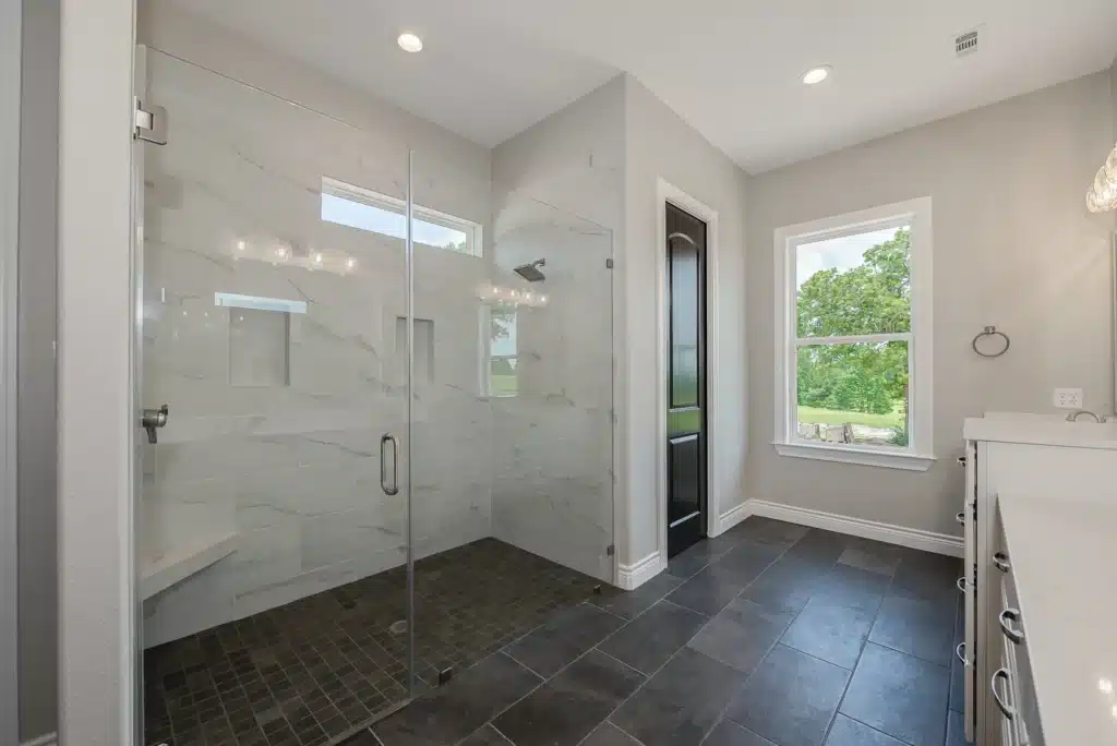 Current image: Bright modern bathroom featuring a curbless glass walk-in shower with large-format tile, dark tile flooring, a window with natural light, and clean contemporary finishes.