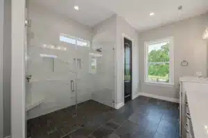 Bright modern bathroom featuring a curbless glass walk-in shower with large-format tile, dark tile flooring, a window with natural light, and clean contemporary finishes.