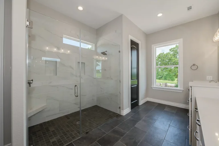 Bright modern bathroom featuring a curbless glass walk-in shower with large-format tile, dark tile flooring, a window with natural light, and clean contemporary finishes.