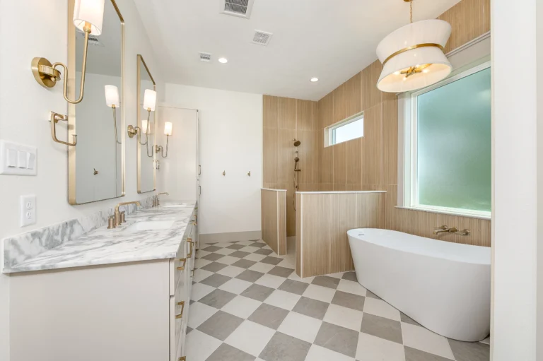 Bathroom with checkered floor, white tub under a window, beige walls, and double vanity with two mirrors and white granite countertops.