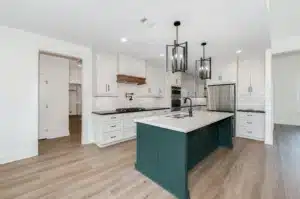 Modern white kitchen with green cabinets, beige wood flooring, fixed round ceiling lights, and sleek white countertops.