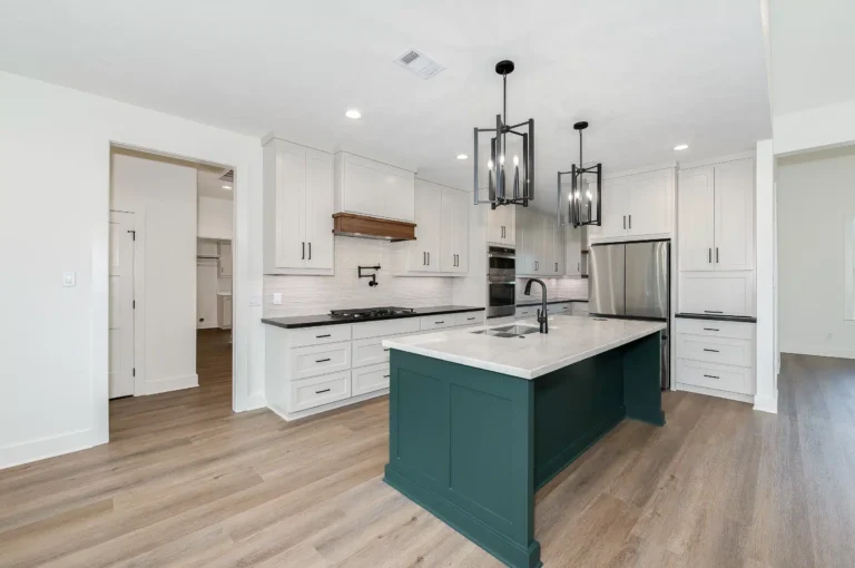 Modern white kitchen with green cabinets, beige wood flooring, fixed round ceiling lights, and sleek white countertops.
