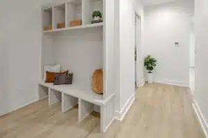 Guest-friendly home entryway with white cubby seating, decorative pillows, light wood flooring, and a corner plant