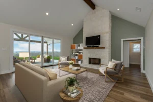 Custom home living room with vaulted ceiling, stone fireplace, wood floors, and large sliding glass doors overlooking the landscape.